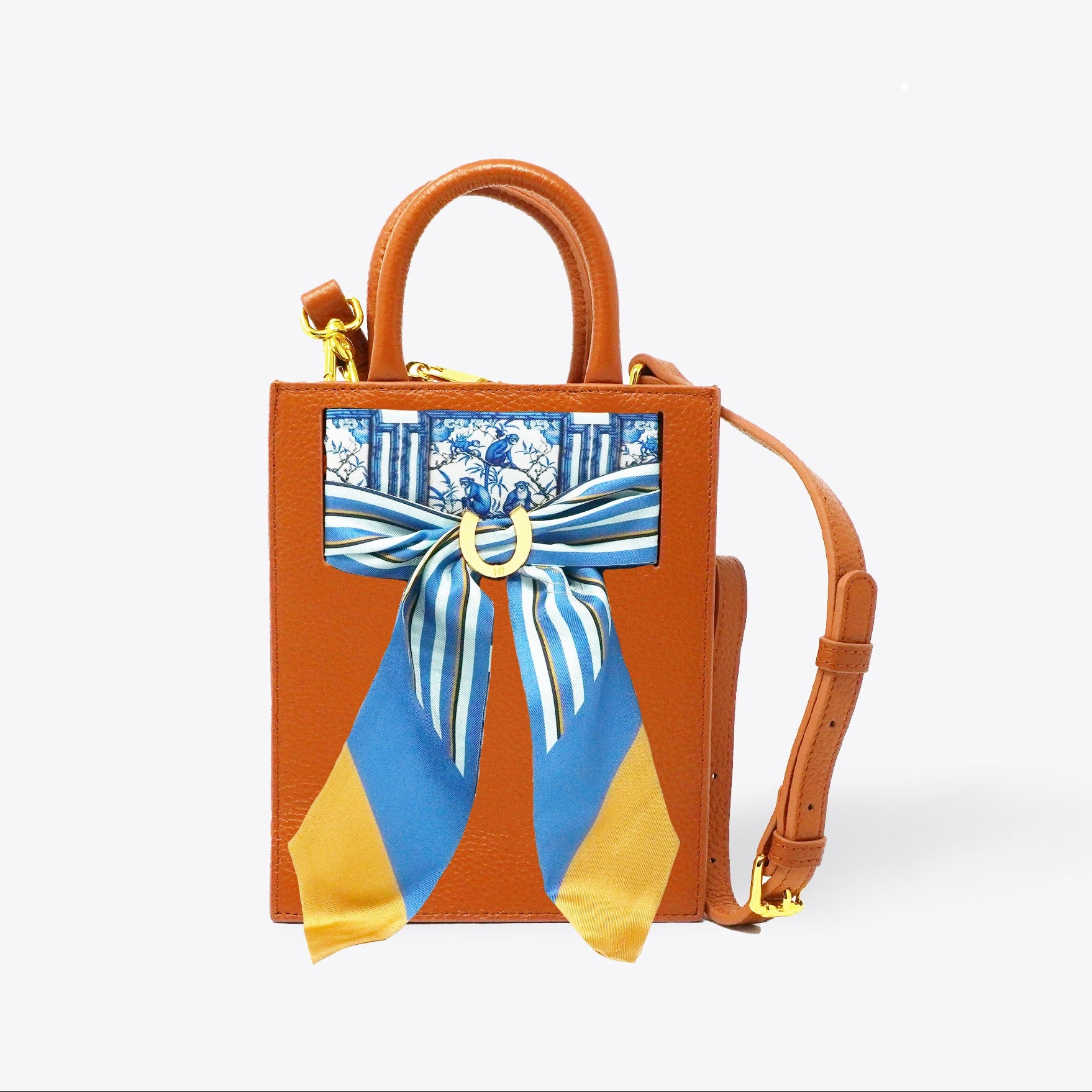 Brown handbag with a blue and yellow scarf tied around it on a white background