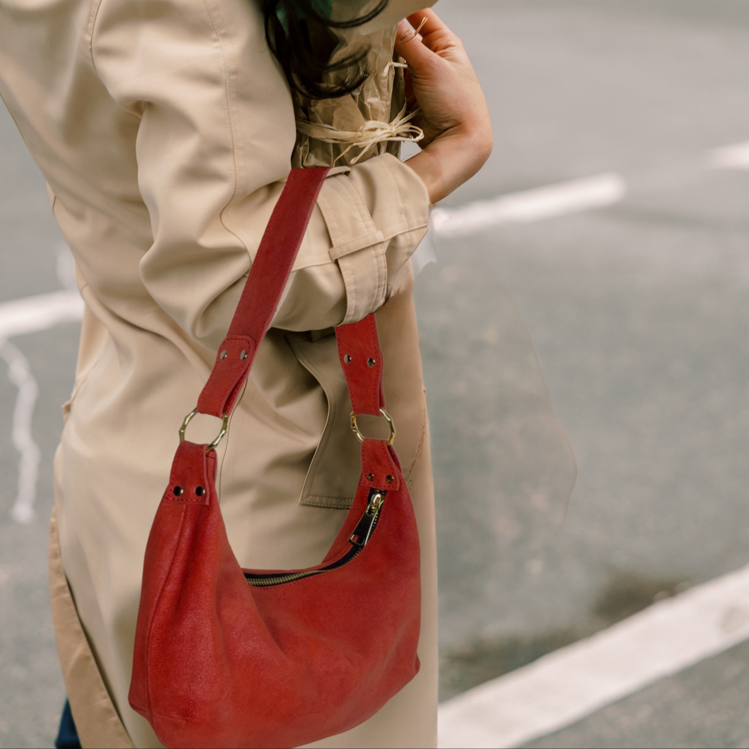 Person holding a bouquet of flowers and a red handbag on a street.