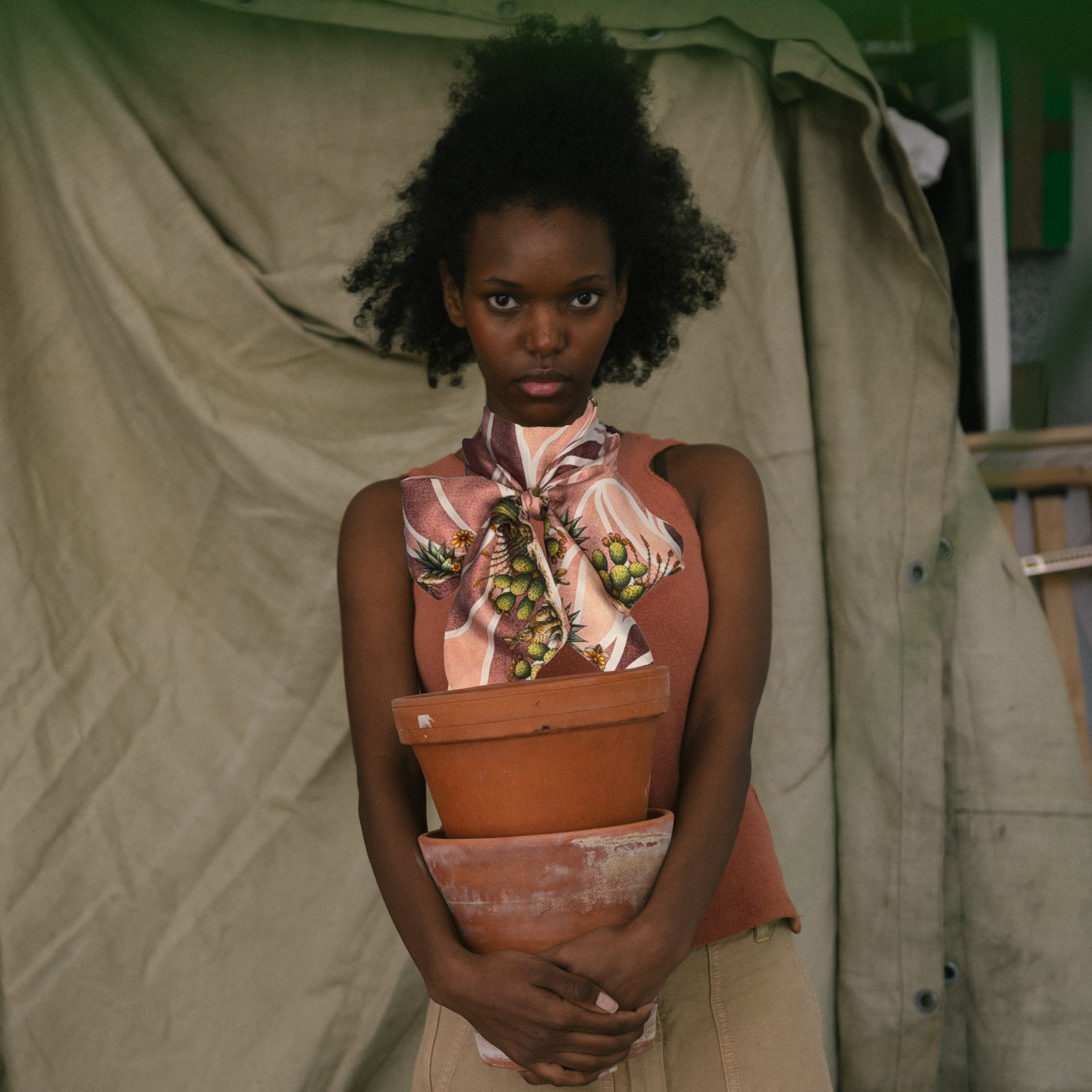 Woman in scarf holding a pot with a plant against a green curtain